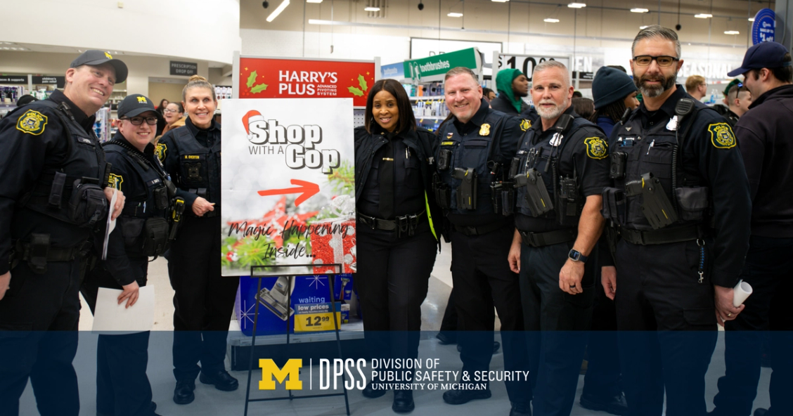 U-M police officers pose with a Shop With a Cop sign.
