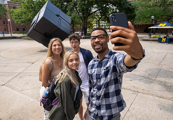 A group of five friends smiling and posing together for a selfie outdoors.